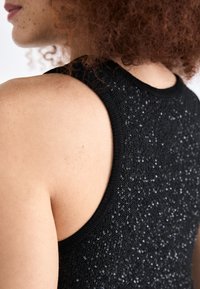 Top nero senza maniche con dettagli in paillettes, realizzato in un materiale a maglia testurizzato e con una vestibilità aderente intorno alle spalle e al collo.