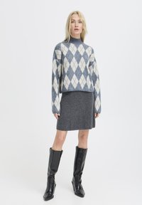 Maglione lavorato a maglia con un motivo a rombi blu e bianchi, abbinato a una gonna grigia e stivali neri sopra il ginocchio, con una vestibilità rilassata e un collo alto.