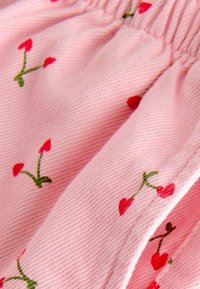 Tessuto rosa testurizzato con motivi di ciliegie ricamati in rosso. Presenta una vita elasticizzata arricciata e un materiale morbido e leggero.
