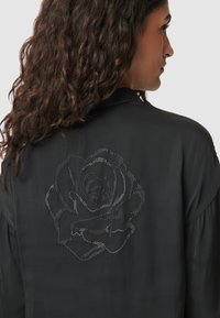 Czarna bluzka z wzorem róży wyszczotkowanym srebrnymi cyrkoniami na plecach, o gładkiej teksturze i luźnym kroju.