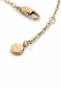 Kuldtooni metallketti koos karabiiniga, millel on ümmargune ripats, millele on graveeritud "Furla". Kujundus on sileda pinnaga ja elegantselt minimalistik.
