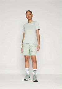 Gaiši zaļš sporta krekls ar īsām piedurknēm un uzrakstu "AWARE", kombinēts ar gaiši zaļām kravas šortiem, kuros ir divas priekšējās kabatas.