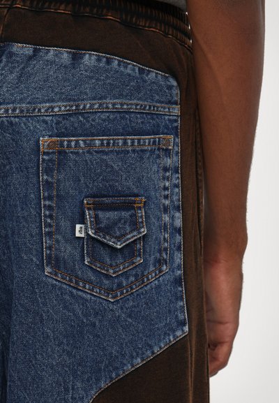 Shorts marron dotés d'une grande poche arrière en denim bleu avec une couture contrastante et une petite poche rectangulaire au-dessus.