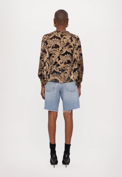 Long-sleeve blouse with intricate gold and black paisley pattern, paired with light denim frayed shorts and black heeled ankle boots.