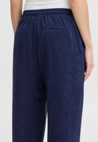 Pantalons en velours côtelé bleu marine avec une taille élastique, comprenant deux poches arrière et une surface douce et texturée. Design à jambe droite.