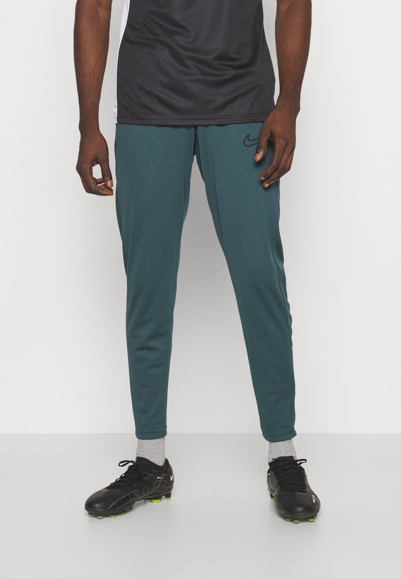 Nike sportbroeken in teal, met een taps toelopend ontwerp, elastische tailleband en zijzakken, gecombineerd met zwarte voetbalschoenen en grijze sokken.