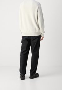 Bílý žebrovaný svetr, černé cargo kalhoty s bočními kapsami a černé boty. Tento outfit se vyznačuje uvolněným střihem a jednoduchým designem.