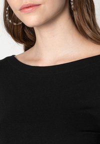 Black, cotton t-shirt with a wide neckline. Notable details include smooth texture and minimal stitching. Silver hoop earring visible.