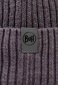 Knitted beanie in dark purple. Features vertical ribbing and a black rectangular label with "Buff" logo sewn on the side.