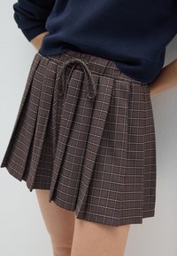Falda de cuadros marrones con pliegues, cintura elástica y detalle de cordón. Presenta un patrón de cuadros sutil en tonos claros y oscuros.