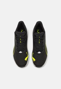 Zapatillas deportivas negras con una parte superior de malla transpirable, acentuadas por un logo y detalles en amarillo neón, con una entresuela blanca y cordones.