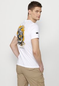 White cotton t-shirt featuring a colorful dragon graphic on the back, with black and yellow accents. Short sleeves, round neckline.