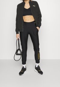 Czarny sportowy zestaw składający się z kurtki na suwak, krótkiego topu, zwężanych spodni z bocznym paskiem oraz czarnych butów sportowych z żółtymi akcentami.