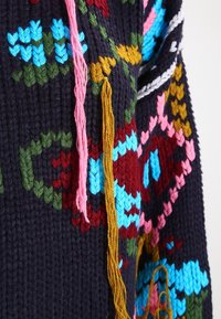 Pletený svetr v tmavě námořnické modři s barevnými květinovými vzory různých motivů. Charakteristické střapce v růžové, žluté a oranžové barvě dodávají texturu.