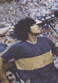 Un hombre lleva una camiseta azul con una franja amarilla horizontal, que presenta rayas blancas a lo largo de las mangas, contra un fondo de multitud borroso.