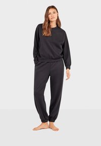 Sort sweatshirt og sweatpants sæt lavet af blødt stof. Har en rund hals, ribbede cuffs, og elastisk talje med ankel-detaljer.