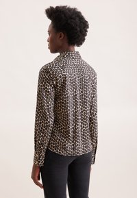 Camicia a maniche lunghe nera con un motivo floreale crema, dotata di colletto classico. Il tessuto ha una consistenza liscia.