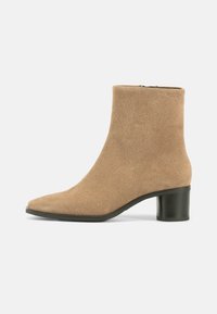 Suede ankle boot in light beige with a pointed toe, discreet zipper, and a chunky black heel for stability. Smooth texture and minimal design.