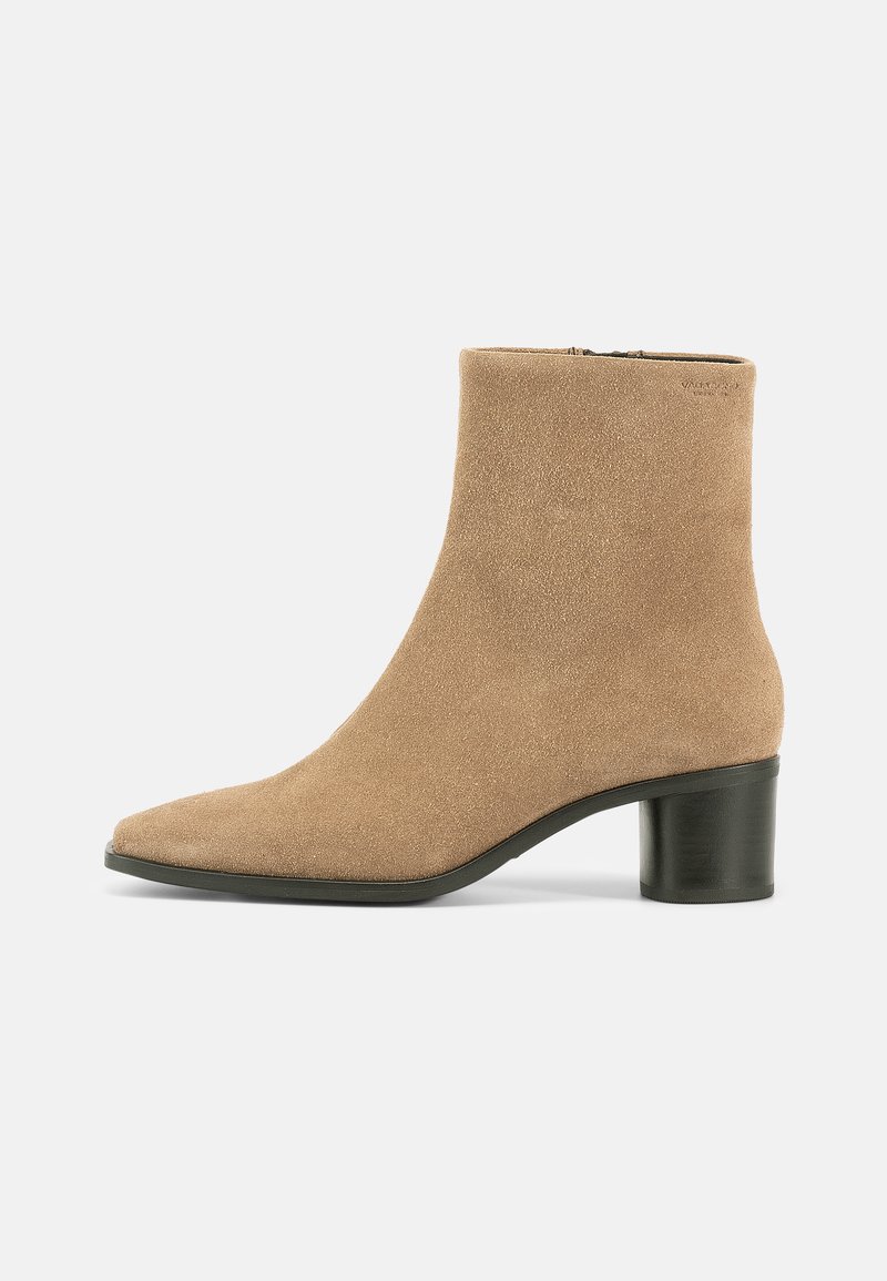 Suede ankle boot in light beige with a pointed toe, discreet zipper, and a chunky black heel for stability. Smooth texture and minimal design.