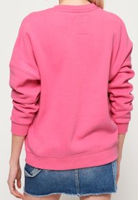 Fuchsia pink sweatshirt with a relaxed fit, ribbed cuffs, and waistband; features a small tag at the neck and smooth fabric texture.