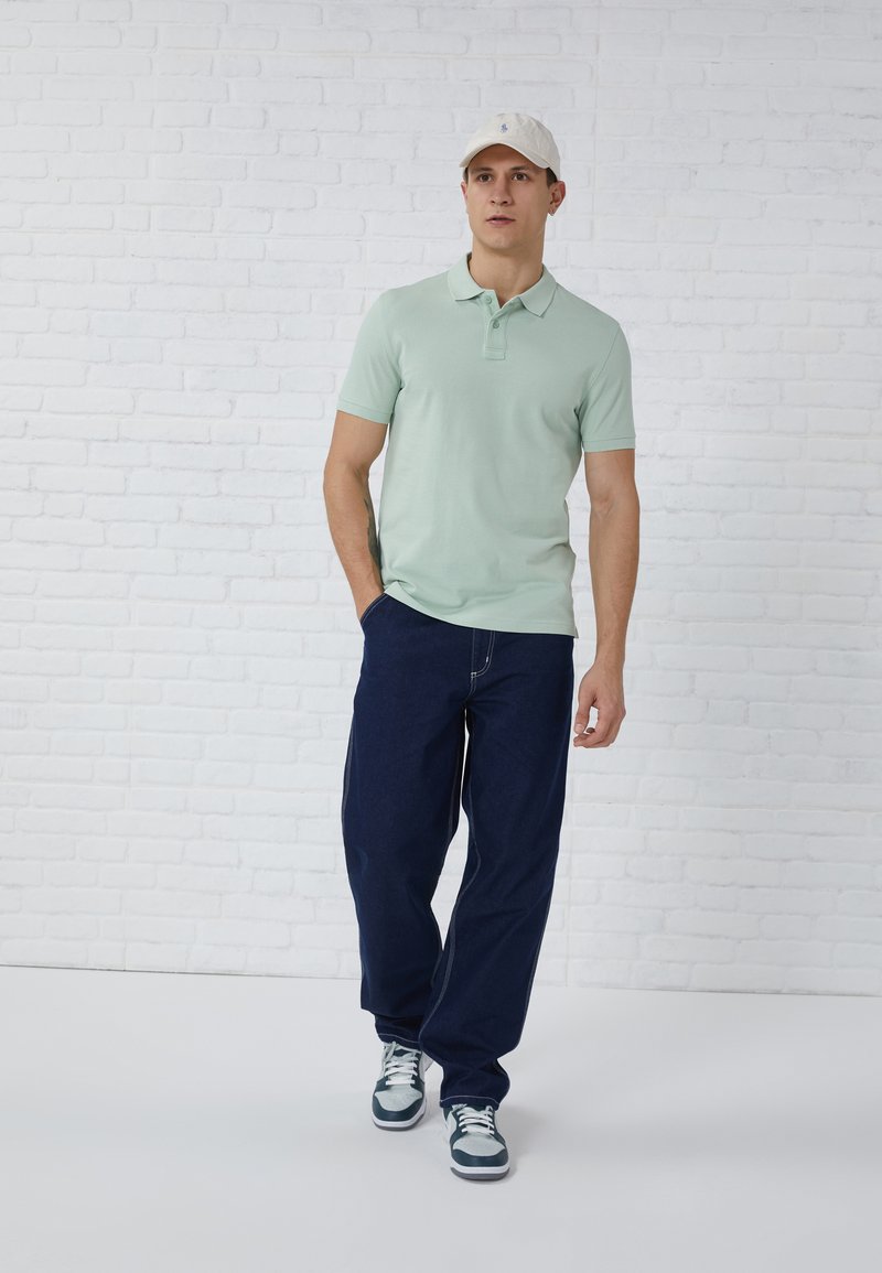 Light green polo shirt with short sleeves, navy blue wide-leg pants, and white cap. Sneakers feature a mix of dark and light blue accents.