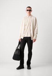 Crème gebreide cardigan met knopen, beige poloshirt, zwarte broek, zwarte sneakers en een zwarte tote bag. Slim-fit design, minimalistische stijl.