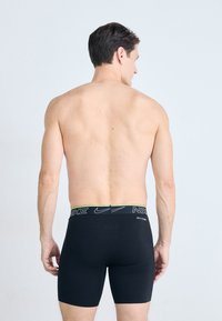 Boxer shorts noirs en stretch avec une ceinture en logo Nike vert et blanc, fabriqués dans un matériau lisse, design ajusté et longueur mi-cuisse.