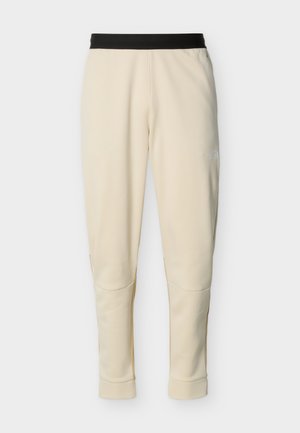 Kreemikas värviga kitsenevad püksid musta elastse vöökohaga ja peen logo ülemise vasaku reie kohal.