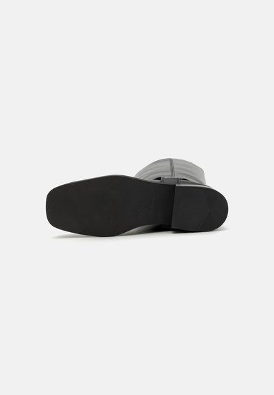 Bota gris con una parte superior de cuero liso, tacón rectangular y suela de goma negra sólida. Presenta un detalle de costura en el empeine.