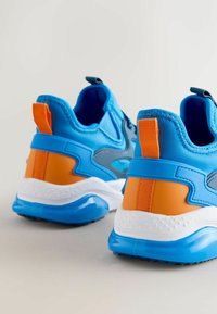 Zapatillas azules con una textura suave, detalles en naranja, un cuello acolchado y una suela blanca con detalles texturizados.