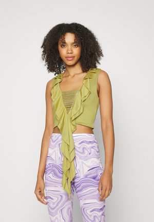 Top verde, cropped, com bordas em babados e um centro metálico texturizado; combinado com calças roxas em mármore de cintura alta. Tecido suave, design ajustado.