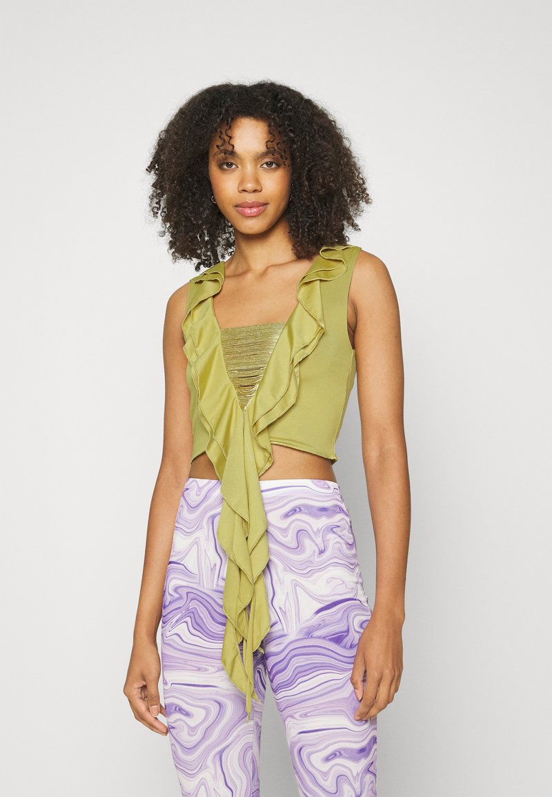 Top verde, cropped, com bordas em babados e um centro metálico texturizado; combinado com calças roxas em mármore de cintura alta. Tecido suave, design ajustado.