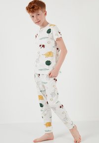 Puuvillainen pyjama, jossa on värikkäitä eläin- ja puukuvioita valkoisella taustalla; lyhythihainen paita ja pitkät housut, joissa on joustava vyötärö.