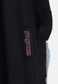 Black backpack made of durable fabric, featuring a blue Jansport logo patch and mesh side pockets. Structured design with sturdy straps.