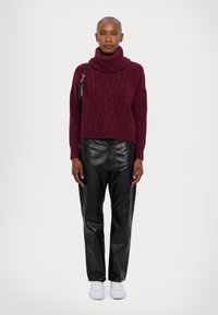 Burgundska pletena turtleneck pulover, v kombinaciji s črnimi usnjeni hlačami in belimi supergami. Eleganten dizajn z vidno pletenjem.
