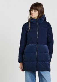 Giacca a vento imbottita blu marina con zip frontale, cappuccio e motivo trapuntato orizzontale. Realizzata in materiale leggero e liscio; presenta maniche lunghe.