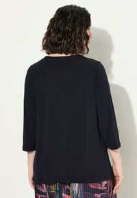 Musta, kevyt yläosa, jossa on kolme neljännesosakäsivartta, pyöreä kaula-aukko ja rento malli; päällä värikkään kuvioidun hameen yli.