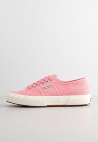 Różowe niskie trampki z płótna z białą gumową podeszwą, metalowymi oczkami i widoczną metką marki Superga z boku.