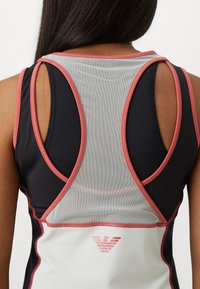 Top de desporto atlético preto e cinza com costas em malha, detalhes em rosa e decote redondo. Apresenta um logo perto da bainha.