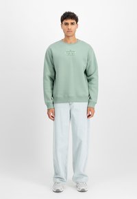 Zielona bluza z długim rękawem, ściągacze przy mankietach i u dołu. Nadrukowane logo na klatce piersiowej. Połączona z jasnoniebieskimi, luźnymi dżinsami i szarymi trampkami.