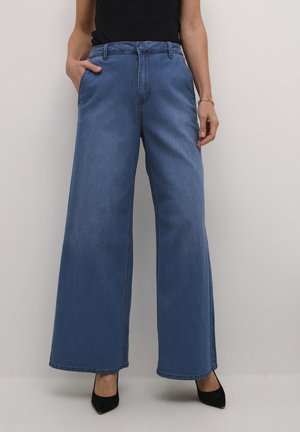 Wijdvallende blauwe denim broek met een hoge taille, voorzien van zijzakken en contrasterende stiksels, gecombineerd met zwarte puntige schoenen.