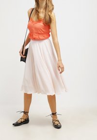 Korallfärgad ärmlös topp med spetsdetaljer, ihopparad med en flödande, ljusrosa midikjol och svarta ballerinaskor med korsade remmar.