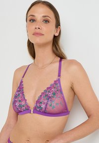 Soutien-gorge en dentelle violette avec des bonnets triangulaires, broderie florale en vert et rose, bretelles ajustables et un détail de fermoir doré au centre.