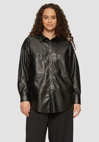 Zwarte faux leren shirt met een gekraagde halslijn, knoopsluiting aan de voorkant en twee voorzakken; heeft een ontspannen pasvorm en een gladde textuur.
