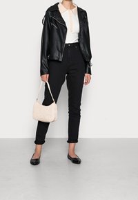 Schwarze Lederbikerjacke über einem weißen gerippten Polohemd mit einem Pfirsichfarbigen Kragen, kombiniert mit schwarzen hochgeschnittenen Jeans und einer beigefarbenen strukturierten Handtasche.