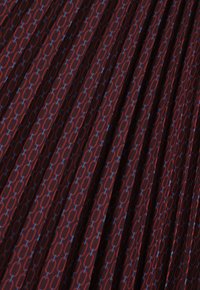 Roter Stoff mit einem geometrischen Muster aus ineinandergreifenden Formen in Blau. Das Material scheint weich mit einer plissierten Textur zu sein.