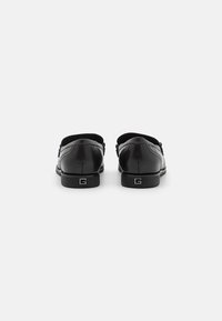 Scarpe di pelle nera con finitura liscia, punta arrotondata e tacco basso. Presentano una sottile cucitura e un logo sul tacco.