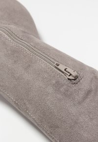 Tela de ante gris con una textura suave, que cuenta con una cremallera visible y costuras a lo largo de su lateral.