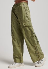 Olijfgroene cargo broeken met een losse pasvorm, voorzien van ritszakken, een verstelbare zoom en een gestructureerde stof. Gepaard met witte sneakers.