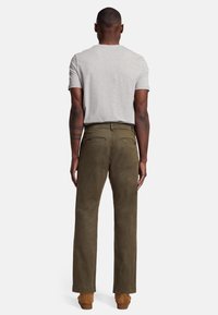 Pantaloni in corduroy verde oliva a gamba dritta, con una texture morbida, dotati di tasche posteriori e chiusura con zip frontale. Indossati con una maglietta grigia.